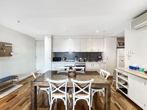 Una cocina moderna con armarios blancos, una mesa de comedor con sillas blancas y piso de madera.