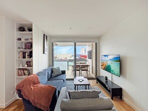 Una sala de estar moderna con sofá, mesa de centro, televisor, estantería y balcón con vista a la ciudad.