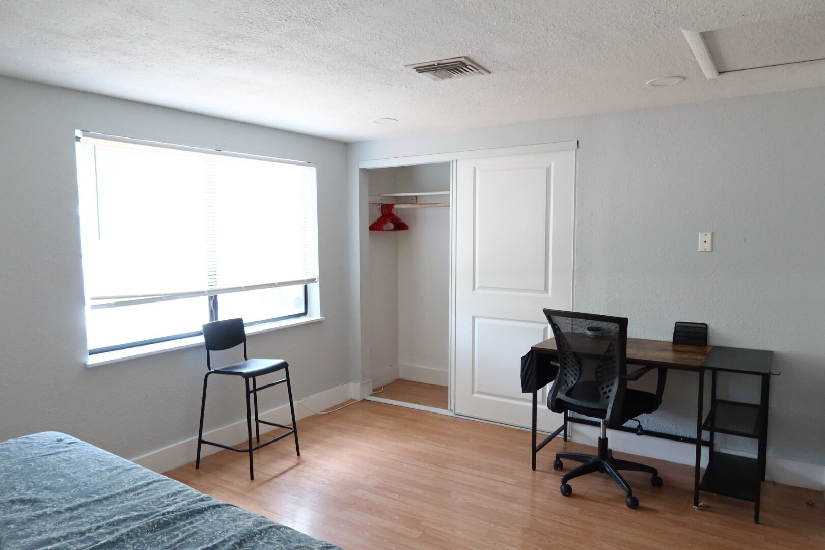 A room with a bed, a desk with a chair, a window, and a door.