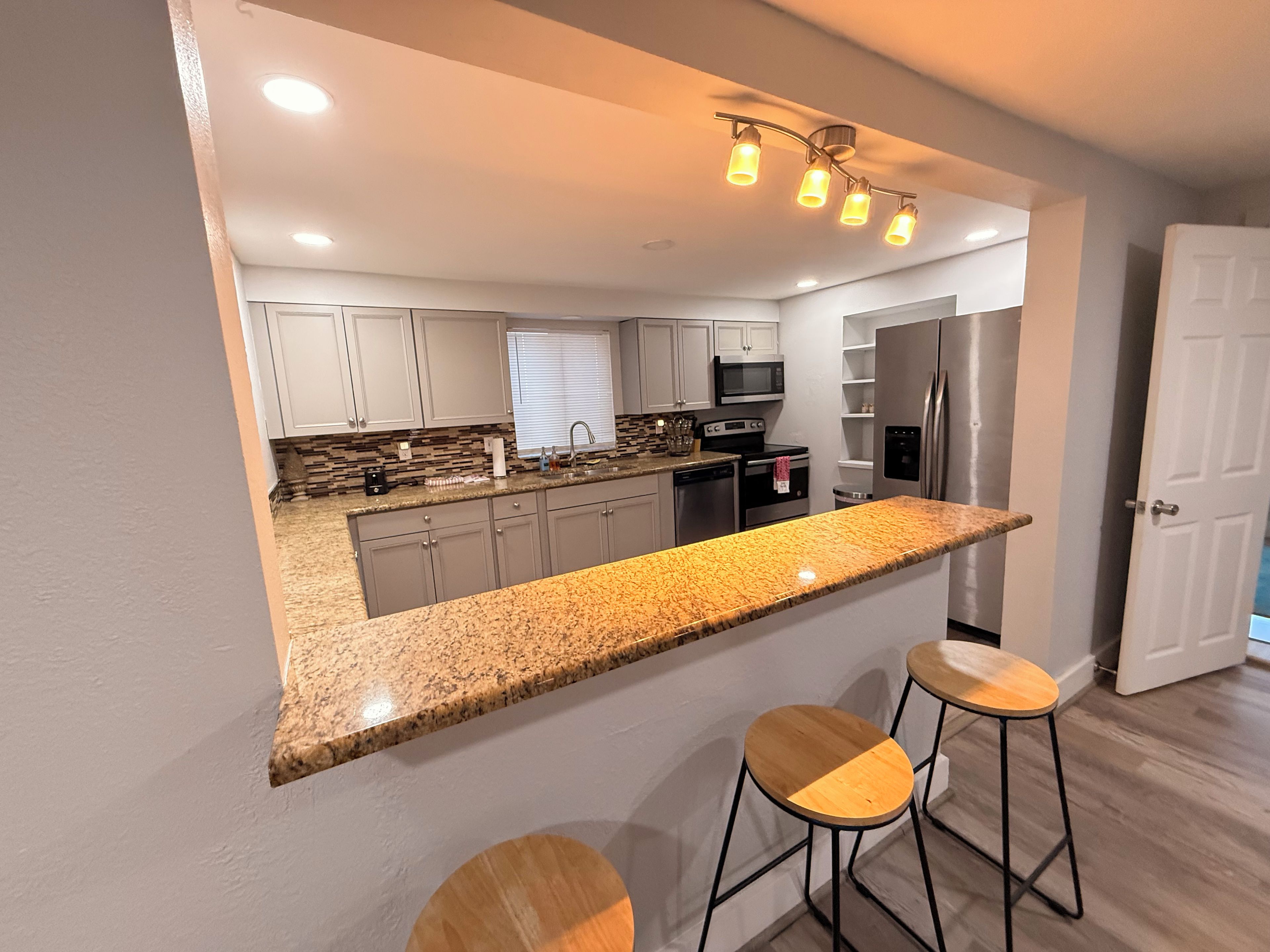A modern kitchen with a granite countertop, stainless steel appliances, and a bar stool seating area.