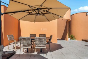 An outdoor patio with a table and chairs, a large umbrella, and a wall with a logo. - Ixuh Ocean Front 5 Ave Playa del Carmen (Playa del Carmen)