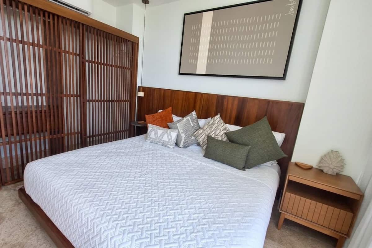 A bedroom with a bed, wooden headboard, and a wall-mounted artwork.