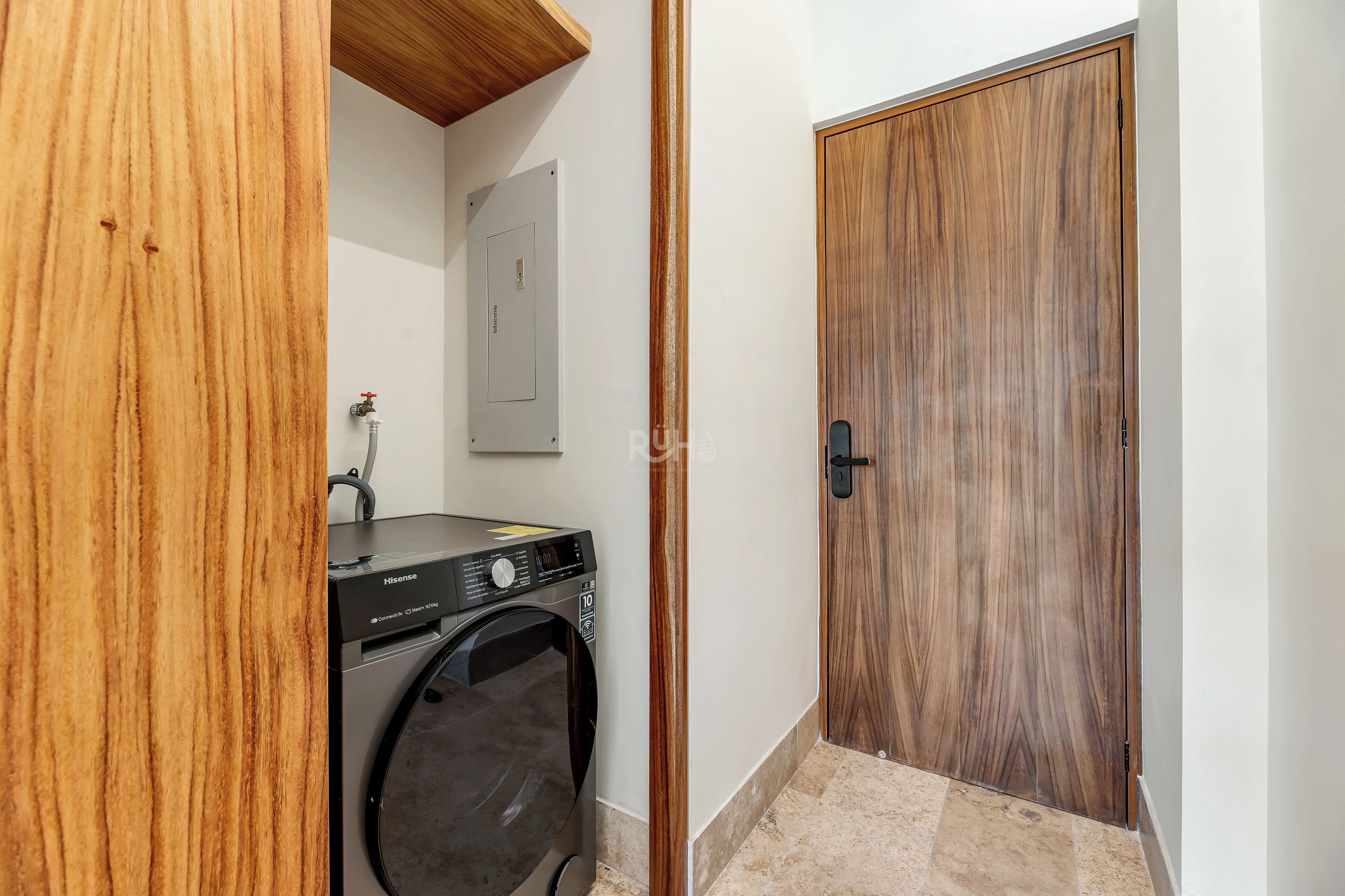 A laundry room with a washing machine, a wooden door, and a white wall.