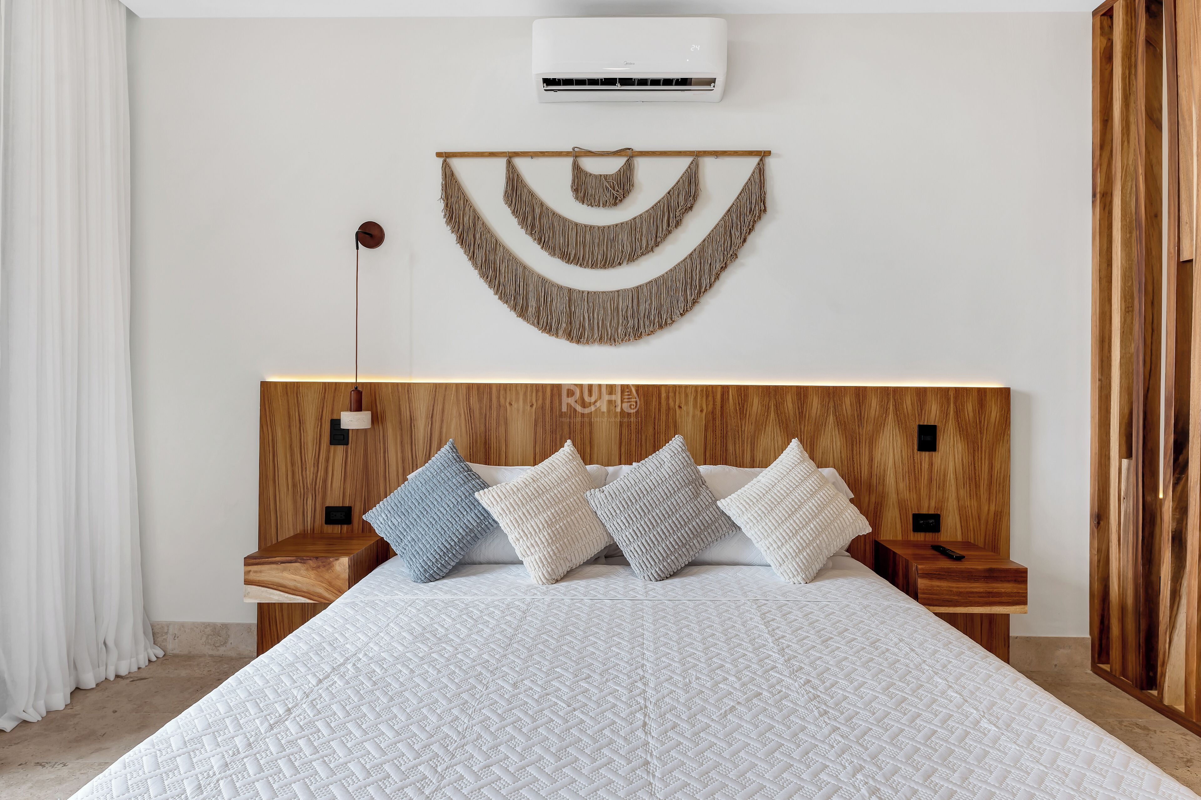 A bedroom with a large bed, wooden headboard, bedside tables, and a wall-mounted air conditioner.