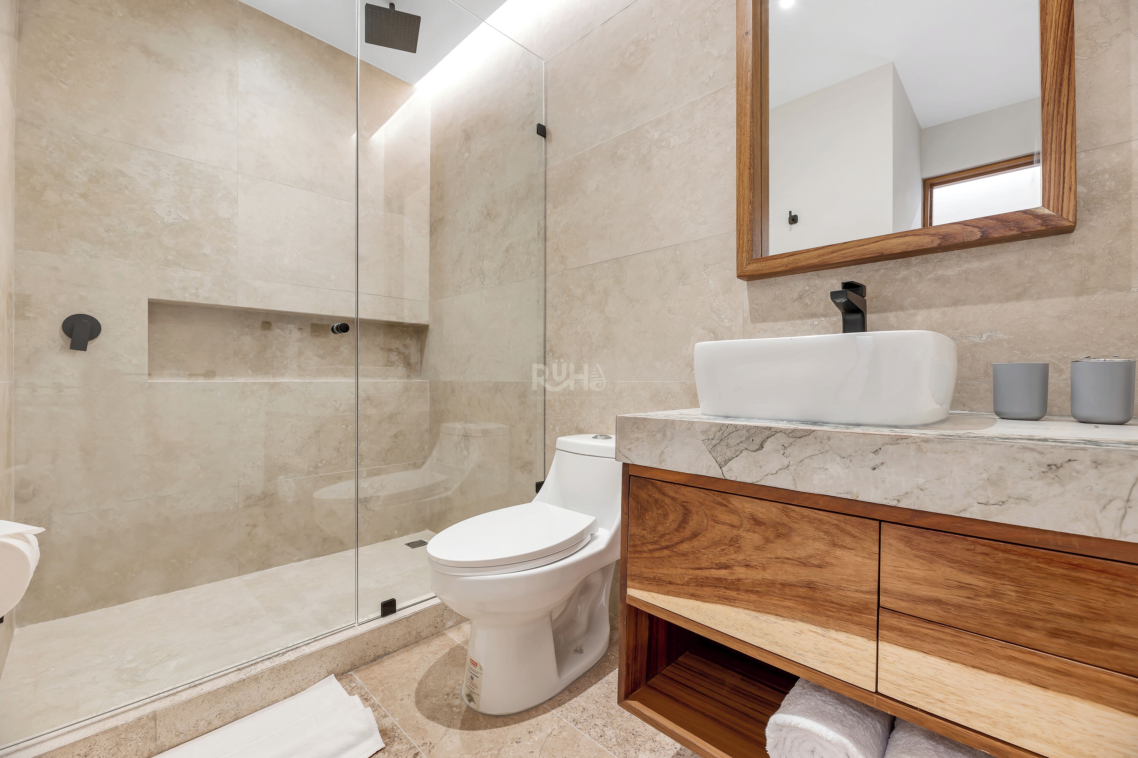 A modern bathroom with a glass-enclosed shower, a white toilet, a marble sink, and wooden cabinetry.