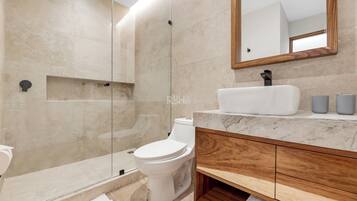 A modern bathroom with a glass-enclosed shower, a white toilet, a marble sink, and wooden cabinetry.