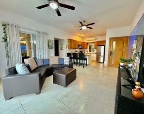 A modern living room with a sectional sofa, a coffee table, and a dining area with chairs. There is a kitchen with a refrigerator and a microwave. - CASA COCO-VISTA Superior 2 Bedroom @ Casa Linda (Sosúa)