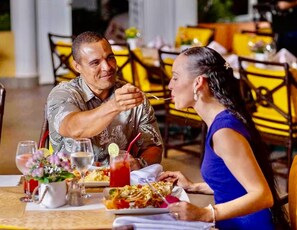 A dining table with a man and a woman eating, a glass of red drink, and a white pitcher with flowers. - CASA COCO-VISTA Superior 2 Bedroom @ Casa Linda (Sosúa)