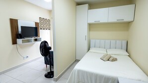 Een hotelkamer met een bed, een televisie, een ventilator en een kledingkast.
