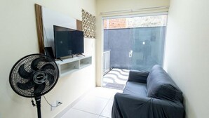 Een woonkamer met een televisie, een ventilator, een bank en een schuifpui naar een balkon.