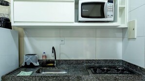 Een kleine keuken met een magnetron, een spoelbak en een gasfornuis.