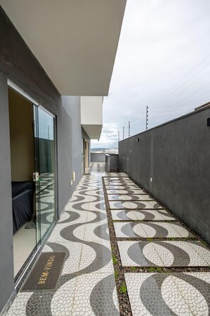 Un pasillo con piso estampado, una puerta de cristal y un felpudo con el texto 'BEM VINDO'.