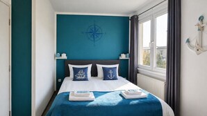 Une chambre avec un lit, une fenêtre, un décor mural représentant une boussole et une petite table.