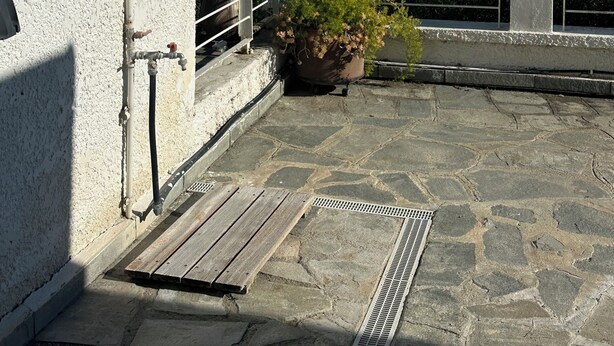 Une terrasse dallée de pierres, avec une rambarde en métal, un pot de fleurs et une vue sur la mer.