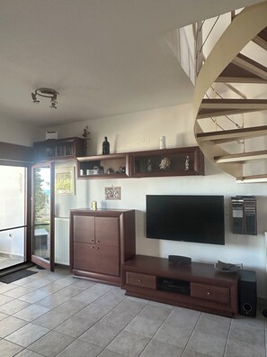 Una sala de estar moderna con televisor de pantalla plana, mueble de madera para entretenimiento y una escalera.