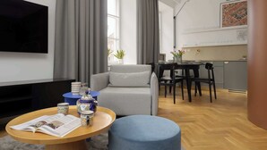 A modern living room with a grey sofa, a wooden coffee table with a magazine, a blue ottoman, and a dining area with a table and chairs. - Atmospheric Apartment in the New Town | Next to the Barbican (Warszawa)