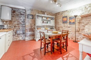 A dining area with a stone wall, a white cabinet with shelves, a table with chairs, and a floor lamp. - Charming 1750 Stonehouse in the heart of Saint Rémy (Saint-Rémy-de-Provence)