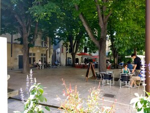 An outdoor café area with tables and chairs, surrounded by trees and buildings. - Charming 1750 Stonehouse in the heart of Saint Rémy (Saint-Rémy-de-Provence)