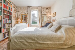 A bedroom with a large bed, a bookshelf, a mirror, and a window with curtains. - Charming 1750 Stonehouse in the heart of Saint Rémy (Saint-Rémy-de-Provence)