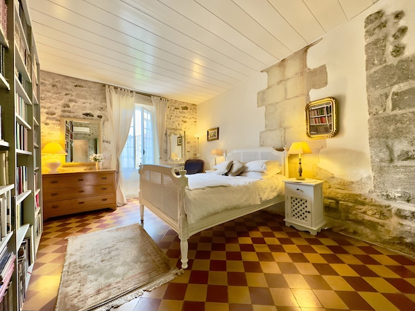 A bedroom with a checkered floor, a bed with white bedding, a dresser, a mirror, and a stone wall. - Charming 1750 Stonehouse in the heart of Saint Rémy (Saint-Rémy-de-Provence)