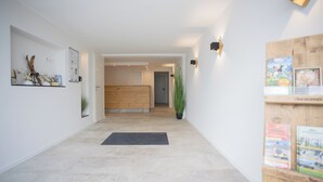 A hallway with a wooden floor, a black doormat, a plant, and a wooden cabinet with books. - Helles und Modernes Appartement (Winterberg)