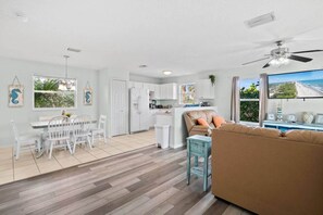 Un amplio salón con una mesa de comedor, muebles blancos, un sofá y vista a la playa.