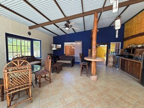 Una habitación amplia con techo alto, ventilador de techo, televisor, zona de comedor con muebles de madera y cocina equipada con estufa y armarios.