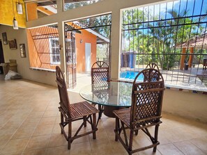 Un área de comedor con mesa de vidrio y sillas de madera, vista a una piscina y un espacio exterior cercado.