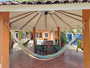 Un porche cubierto con una hamaca, sillas de madera y una piscina.
