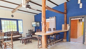 Una habitación con techo alto, televisor montado en la pared, muebles de madera y un ventanal grande.