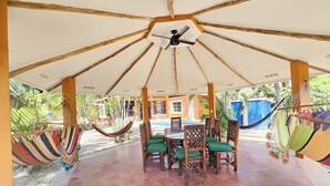 Un espacio al aire libre con techo, piscina, sillas de madera y hamacas.