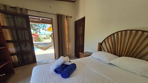 Habitación de hotel con cama, cabecera de madera, puerta de madera y vista al exterior.