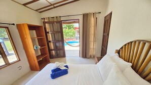 Habitación de hotel con cama, cabecera de madera, estante de madera y vista a una piscina al aire libre.