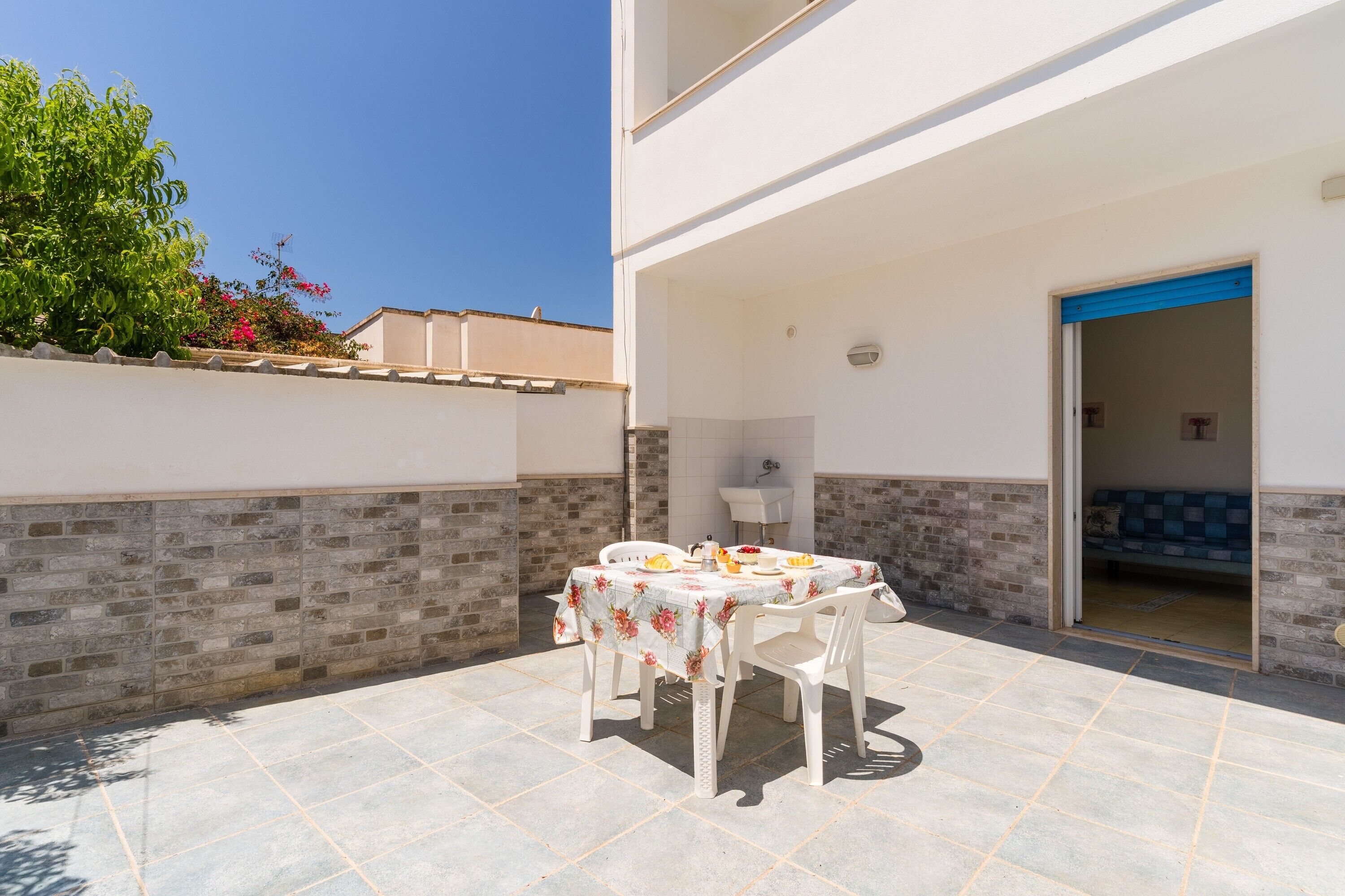 An outdoor patio with a table and chairs, a brick wall, and a door leading to an interior space.
