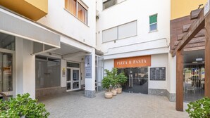 A building with a 'PIZZA & PASTA' sign, a glass door entrance, and potted plants in the courtyard. - Apartment 'Columbia Praia Da Rocha' with Balcony, Wi-Fi, Air Conditioning and garage (Portimão)