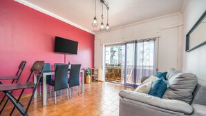A living room with a red wall, a grey sofa, a TV, and a balcony with a view. - Apartment 'Columbia Praia Da Rocha' with Balcony, Wi-Fi, Air Conditioning and garage (Portimão)