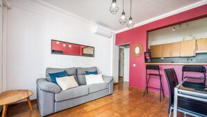 A living area with a grey sofa, a wooden coffee table, a kitchen with wooden cabinets, and a pink accent wall. - Apartment 'Columbia Praia Da Rocha' with Balcony, Wi-Fi, Air Conditioning and garage (Portimão)