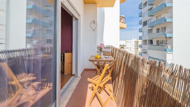 A balcony with a table and chairs, a wooden fence, and a view of neighboring buildings. - Apartment 'Columbia Praia Da Rocha' with Balcony, Wi-Fi, Air Conditioning and garage (Portimão)