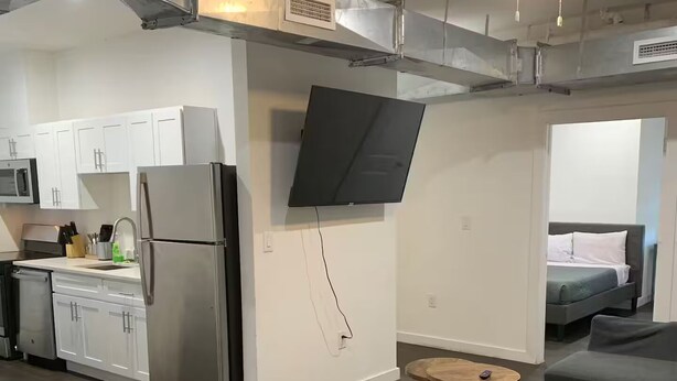 Een moderne keuken met witte kasten, een roestvrijstalen koelkast en een flatscreen televisie aan de muur.
