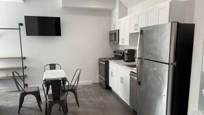 Una cocina moderna con armarios blancos, un refrigerador de acero inoxidable, un microondas y una zona de comedor con mesa y sillas.