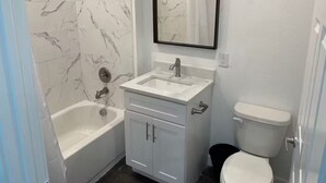 Un baño con bañera, lavabo con espejo y retrete.