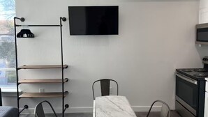 Una cocina moderna con horno integrado, una mesa de comedor con sillas, un televisor montado en la pared y una estantería metálica.