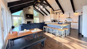 A modern kitchen with a stone fireplace, wooden beams, and a large island with bar stools. - Wide Sky Chateau Lake Views (Osage Beach)