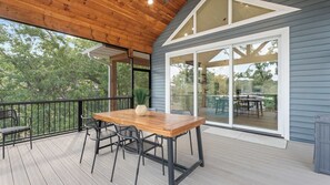 Un patio cubierto con una mesa y sillas de madera, grandes puertas correderas de vidrio y vista a un jardín.