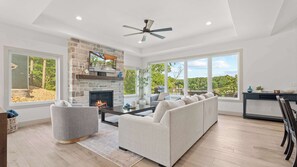 A modern living room with a stone fireplace, a sofa set, and a dining area with a view of the outdoors. - The Blue Sapphire - Dock, Hot Tub & Fire Pit (Sunrise Beach)