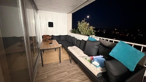 Un balcon avec un canapé noir, une table en bois et un haut-parleur.