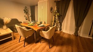 Un coin repas comprenant une table en bois, quatre chaises, un vase avec des plantes séchées, une petite table d’appoint en bois et un canapé.