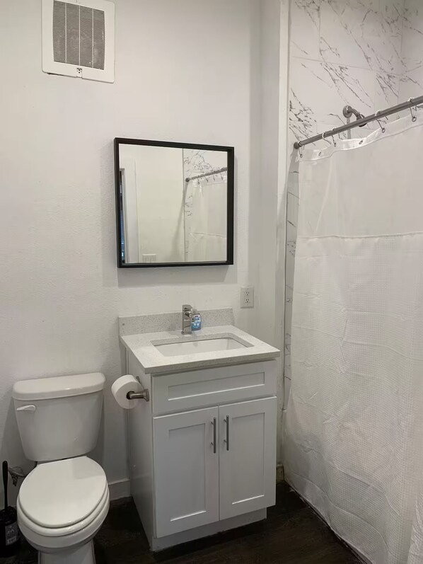 Et badeværelse med toilet, vask, spejl, badeforhæng og en vægventil.