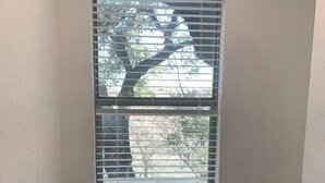 Ein Eckzimmer mit Schreibtisch, Stuhl, Fenster mit Jalousien und einer Topfpflanze.