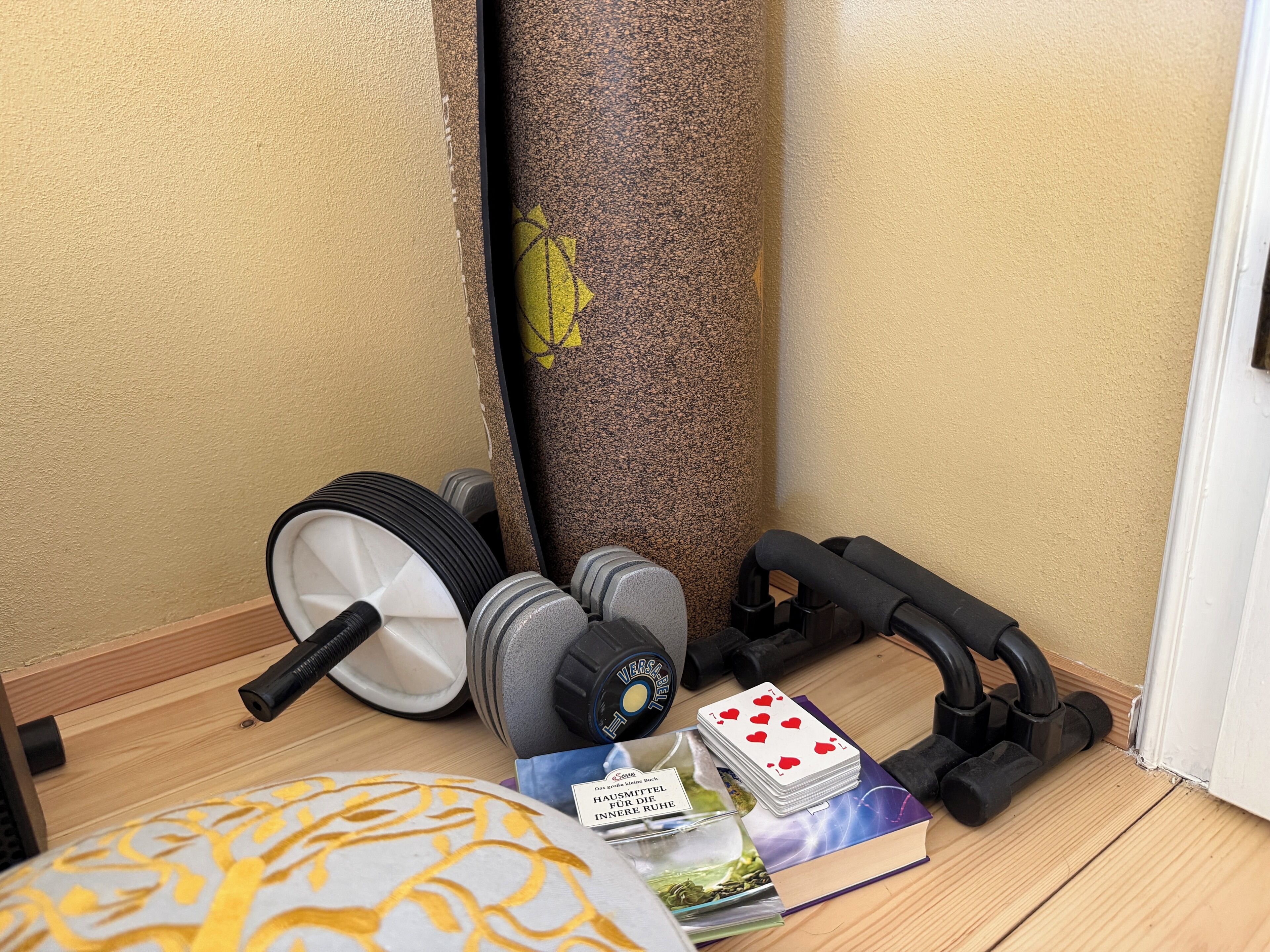 Een hoek van een kamer met fitnessapparatuur, een deur en een houten vloer.